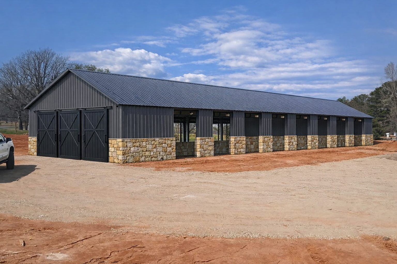 Covered equestrian arena with dark metal siding and stone wainscot